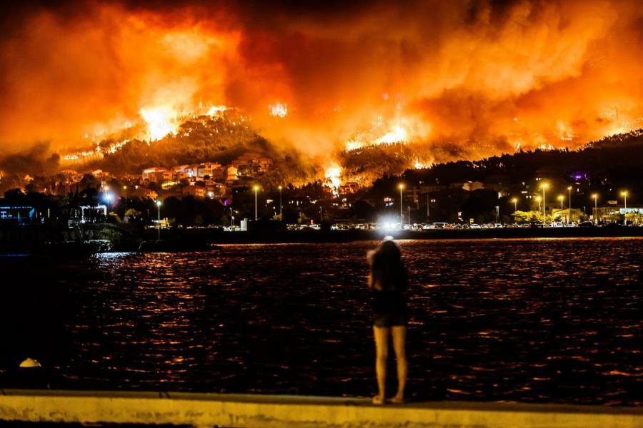 A lady watches over the water as the hillside of Split burns. Image via Damira Kalajzic